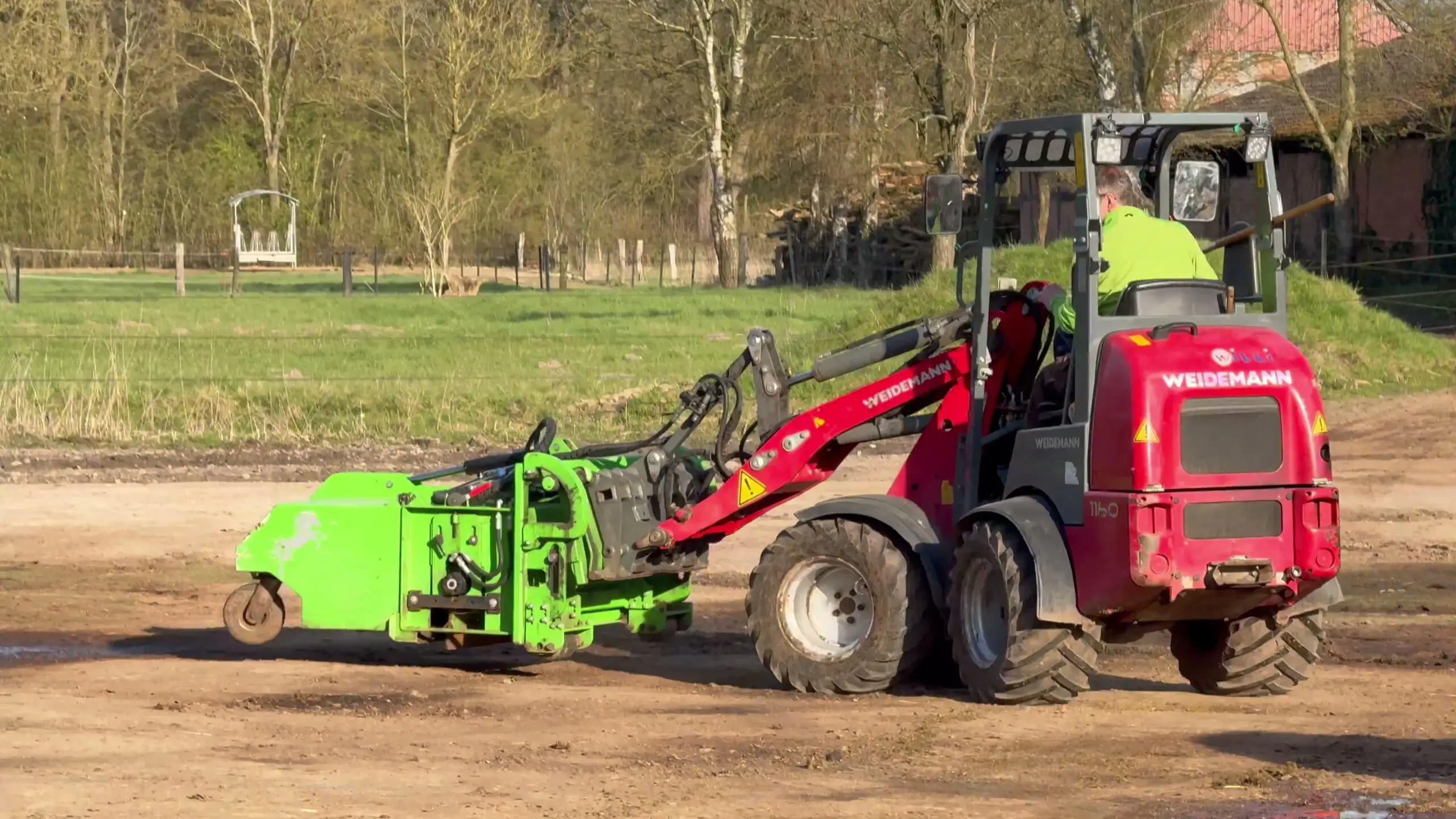 Weidemann-Hoflader mit FARM-SERVANT ECO fährt über den Hofplatz, dahinter Wiese und Bäume